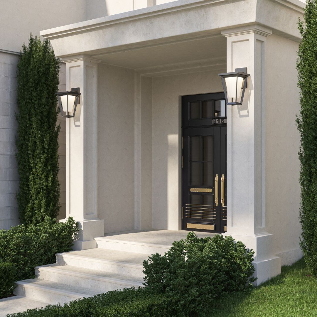 A bright, cream-colored stone entryway with a black front door, flanked by two large, modern black tapered lanterns.