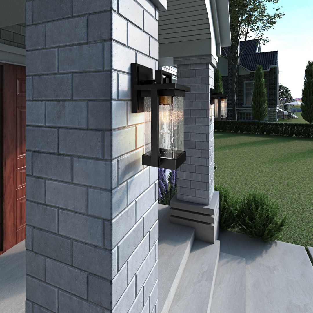 A close-up of a black, rectangular outdoor wall lantern with seeded glass mounted on a light gray brick pillar.